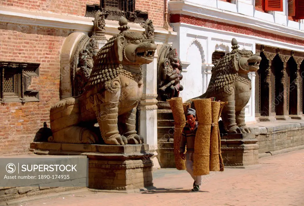 Man carrying coir rugs through the street past ancient statues in Bhaktapur, Nepal