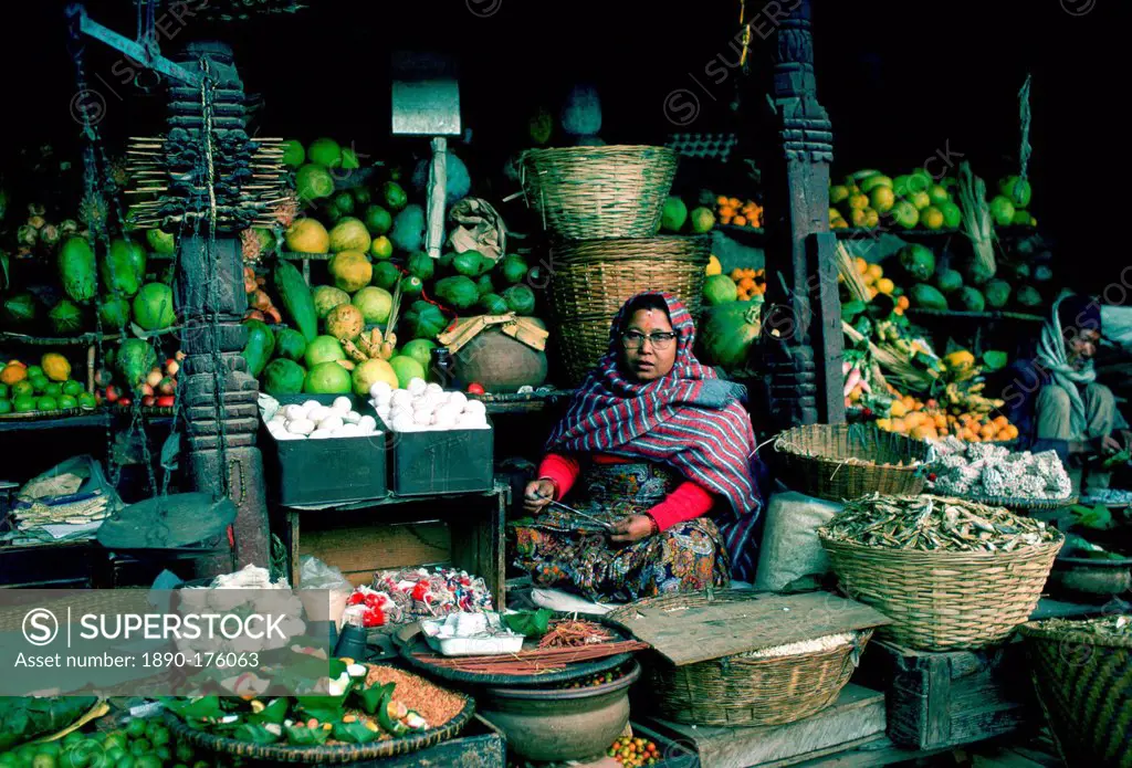 Woman stallholder holding the knife she uses to cut fruit for sale in the market in Kathmandu, Nepal. Her stall displays in baskets fruit, vegetables ...