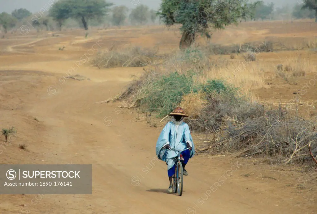 A local man wearing a sunhat rides a bicycle on the road to Sebba through the desert drought areas of Burkina Faso (formerly Upper Volta)