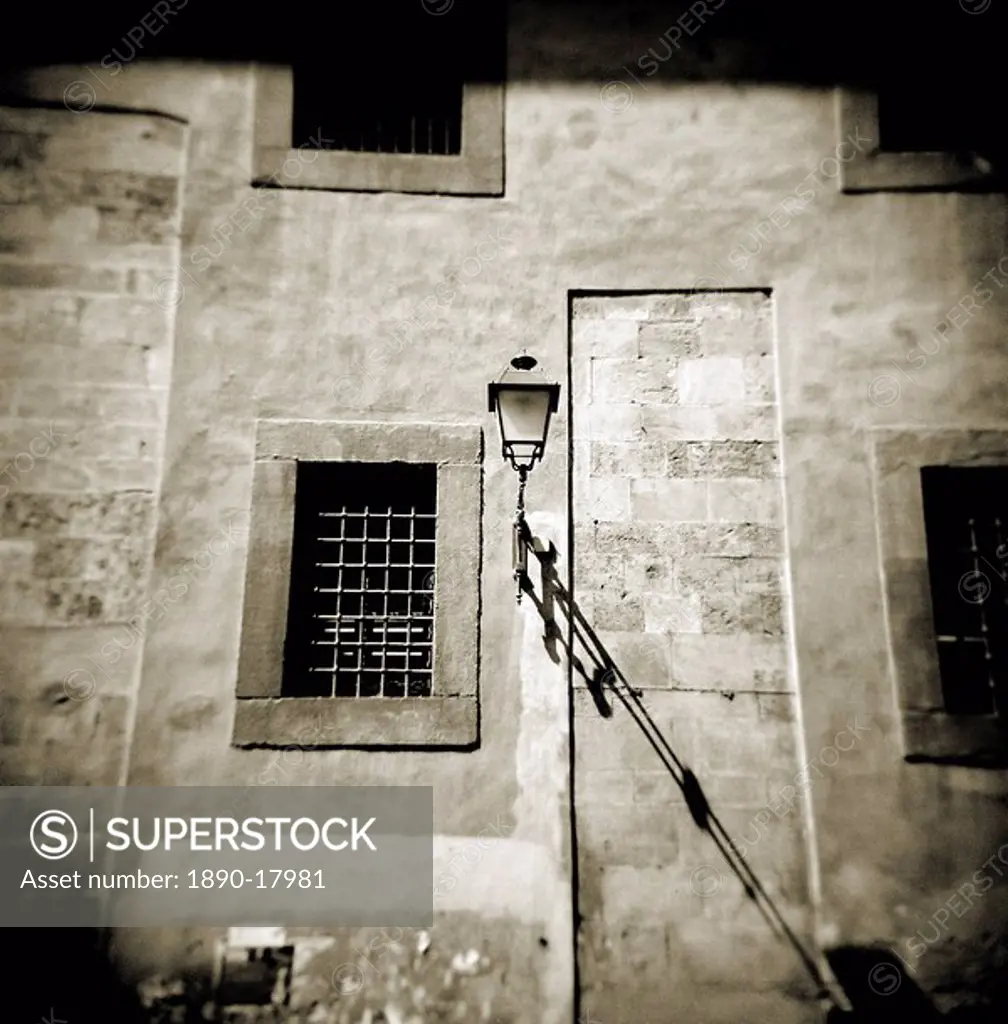 Image taken with a Holga medium format 120 film toy camera of detail on wall of old building showing street lamp, window and shadows, Pisa, Tuscany, I...