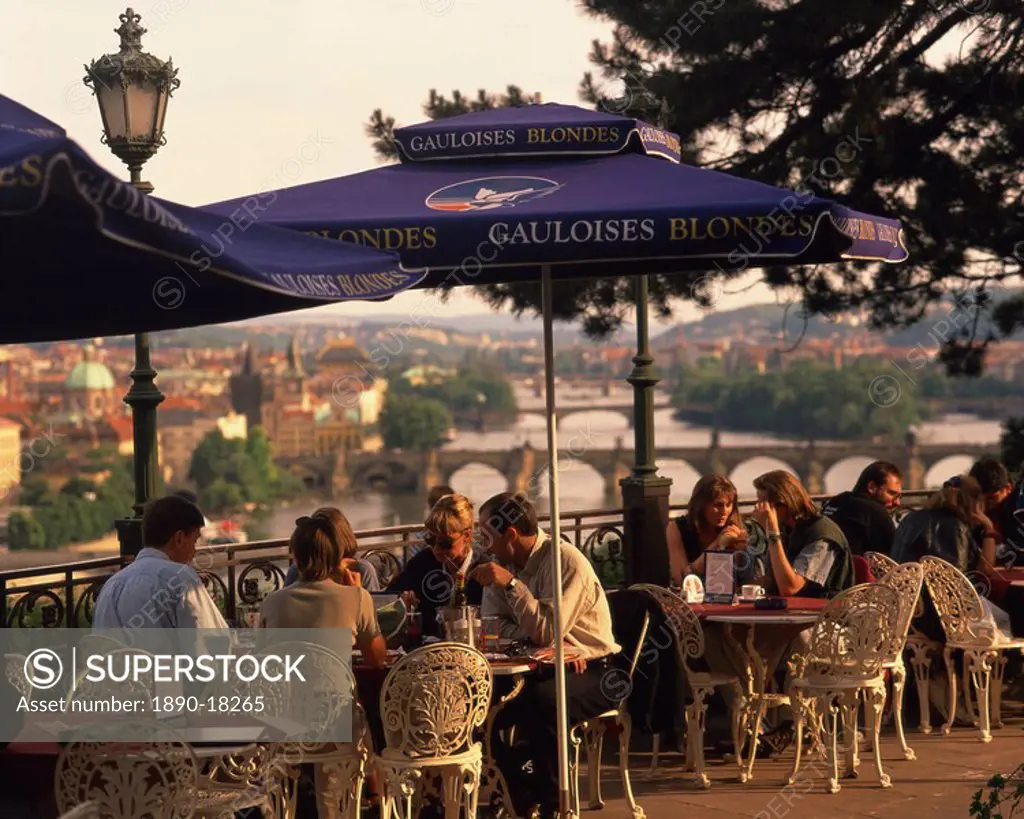People at cafe tables in the open air at the Hanavsky Pavilion, with the river and the city of Prague behind, in The Czech Republic, Europe