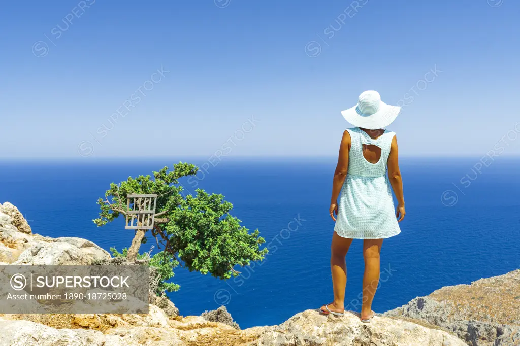 Back view of woman with fashion dress and hat looking at the sea from cliffs, Crete, Greek Islands, Greece, Europe