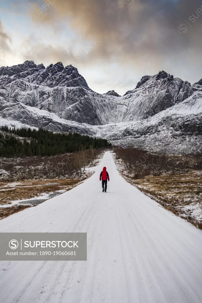 Man walking on empty mountain road covered with snow in winter, Nusfjord, Nordland county, Lofoten Islands, Norway