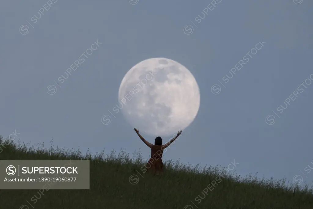 Full moon portrait at blue hour with a girl holding the moon above her head, Emilia Romagna, Italy
