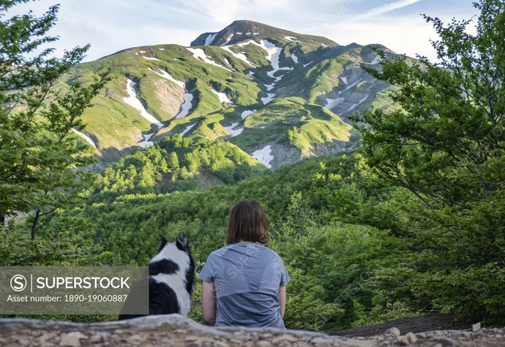 A girl sitting beside her border collie dog staring at a mountain landscape of Cusna Mountain, Emilia Romagna, Italy