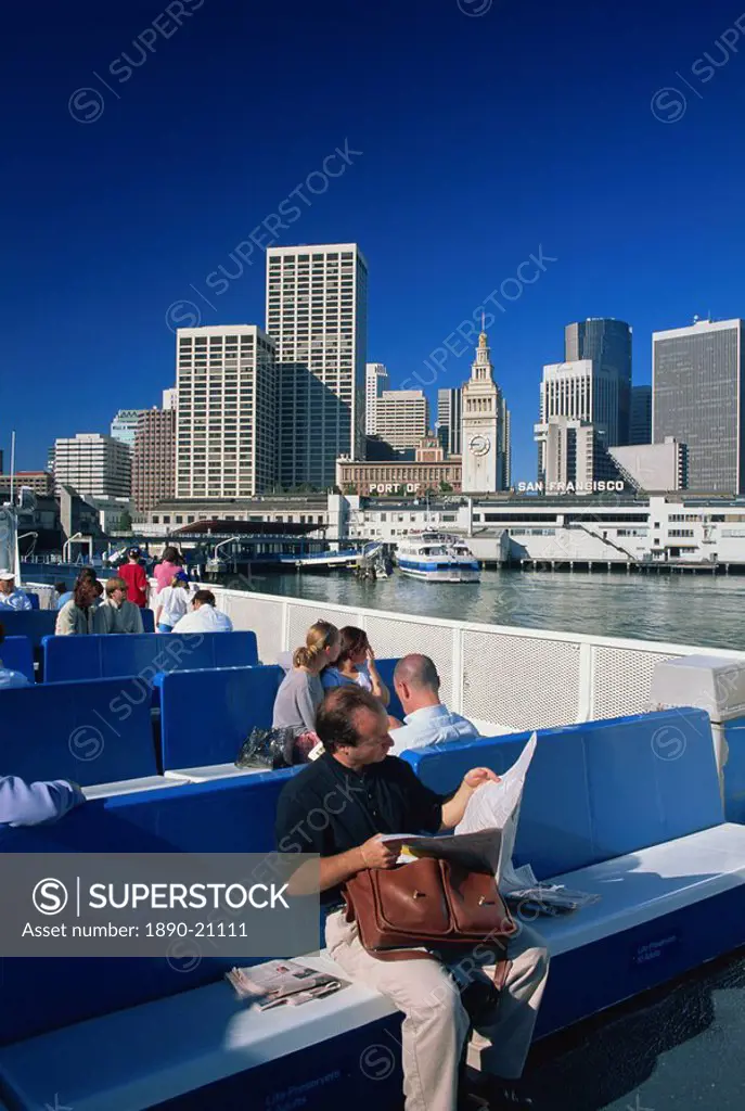 Man reading newspaper and passengers on the commuter ferry, with Ferry Building and skyline of downtown San Francisco in the background, California, U...