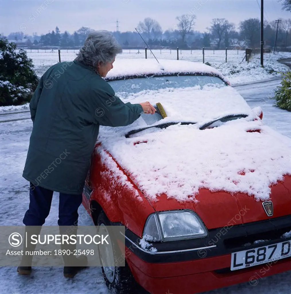 Woman scraping snow off the windscreen of a car in winter, United Kingdom, Europe