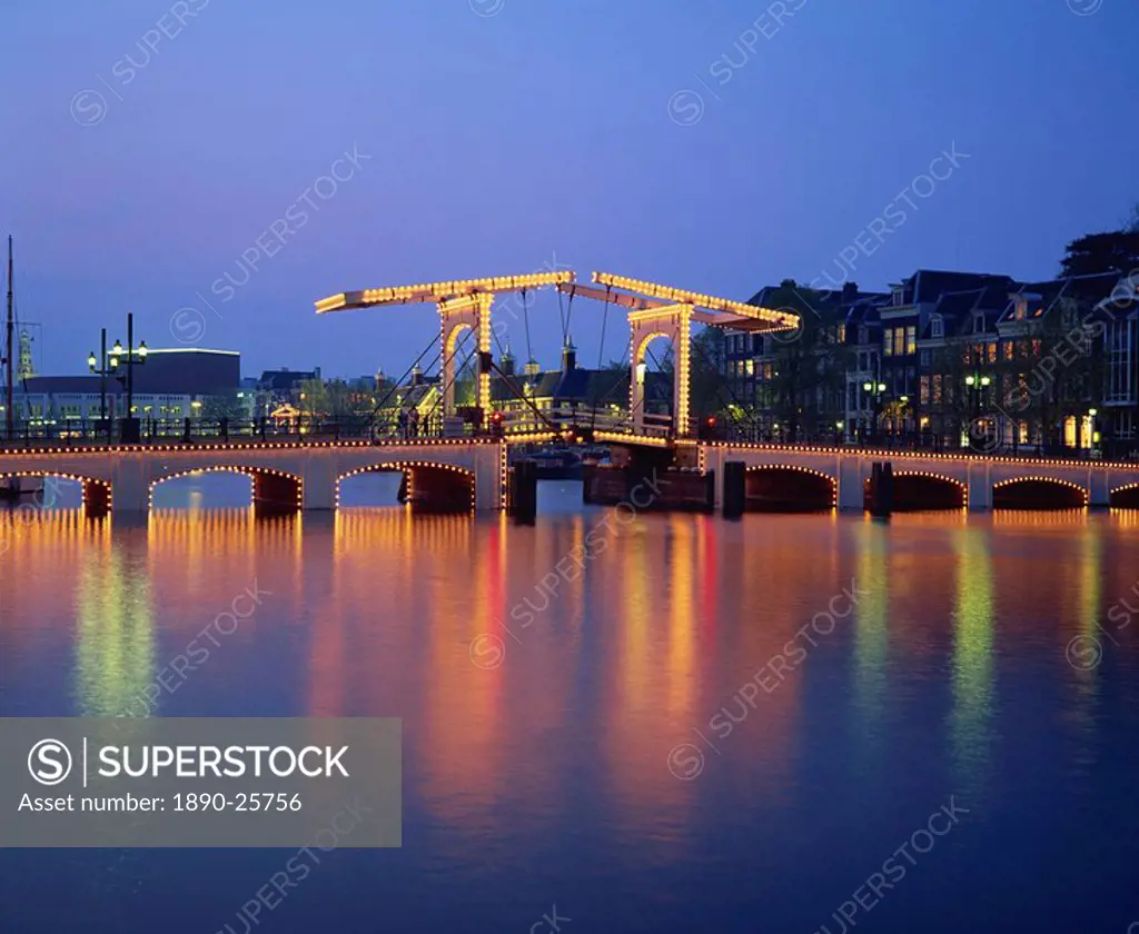 Lights on the Magere Brug Skinny Bridge, reflected in the canal in the evening in Amsterdam, Holland, Europe