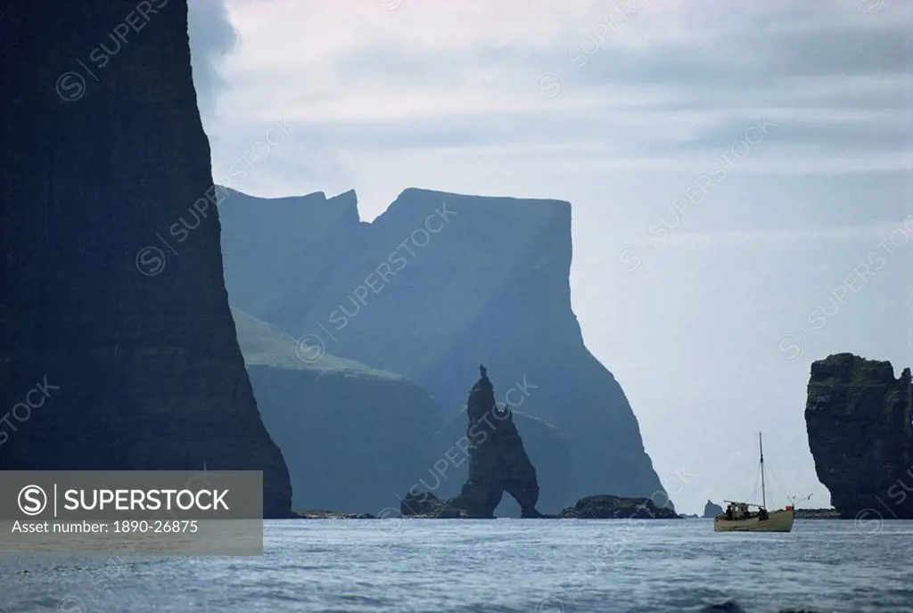 Small fishing boat before a towering cliff coastline, Faroe Islands, Denmark, Atlantic, Europe