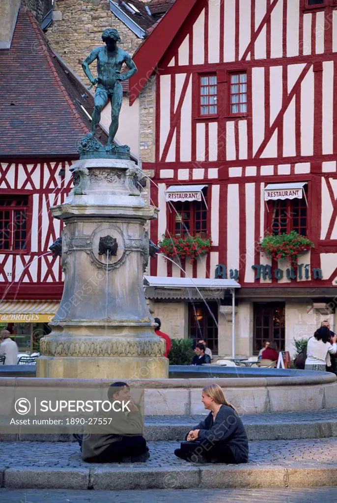A couple sit in front of a fountain in the Place Francois Rude, with half timbered houses behind, in Dijon, Burgundy, France, Europe