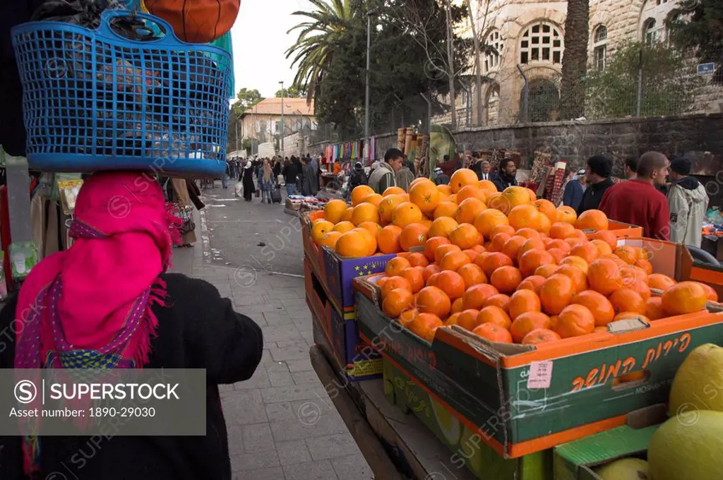 Palestinian woman in colourful scarf and carrying bag on her head walking past an orange stall, Damascus Gate area, Jerusalem, Israel, Middle East