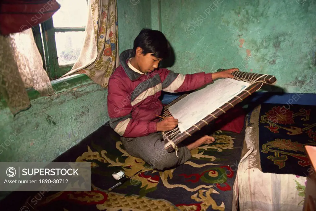 Portrait of a young Tibetan Thangka painter, sitting on a carpet indoors, tangkha paintings used for visualisation in Buddhist meditation, in Darjeeli...