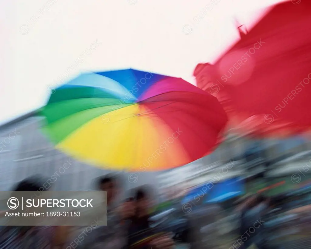 Motion blur image of a brightly coloured umbrella held up against the rain