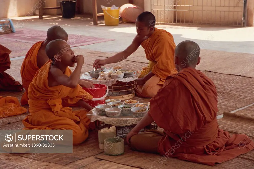 A group of Buddhist monks in saffron robes sitting on the floor, eating, at Wat Chan in Vientiane, Laos, Indochina, Southeast Asia, Asia