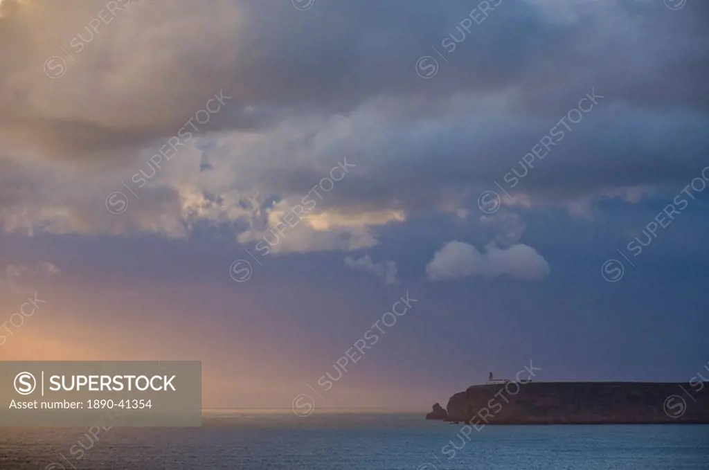 Stormy sunset over Atlantic ocean and cliffs at Cape St. Vincent with lighthouse in the distance, Sagres, Algarve, Portugal, Europe