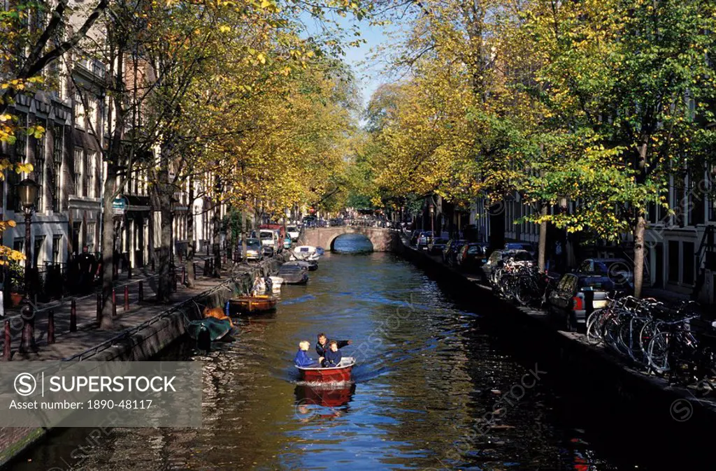 Small boat on tree_lined Oudezijds Achtenburg Wal canal in the autumn, Amsterdam, The Netherlands Holland, Europe