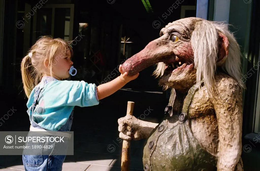 Young girl with dummy in her mouth, touching troll statue with long nose, Norway, Scandinavia, Europe