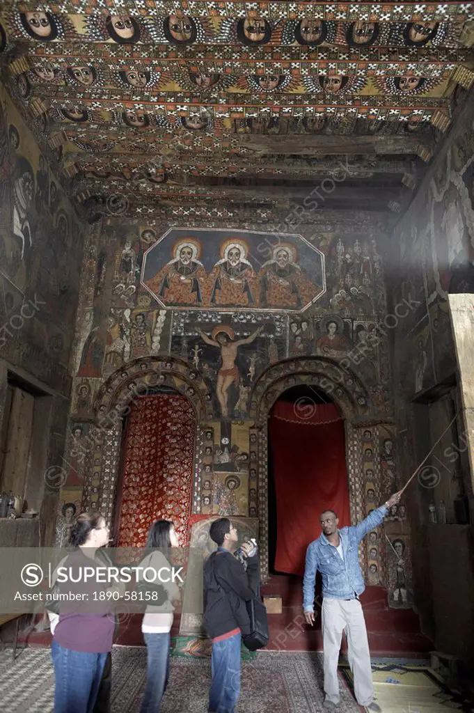 A guide shows tourists the ecclesiastical artwork adorning the walls of Debre Berhan Selassie Church, Gondar, Ethiopia, Africa