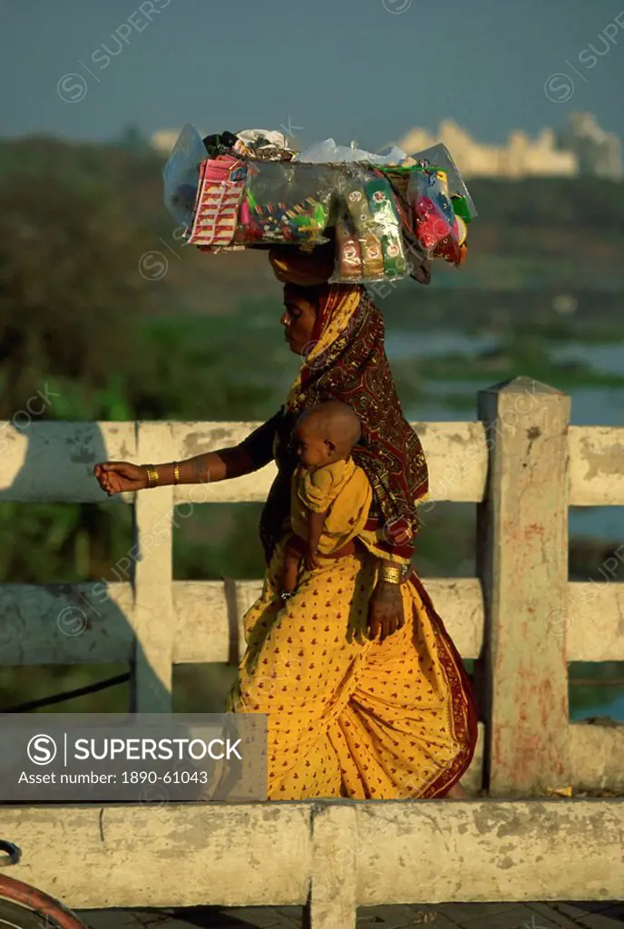 Street vendor carrying her wares and baby crossing the Mula River, Pune, Maharashtra state, India, Asia
