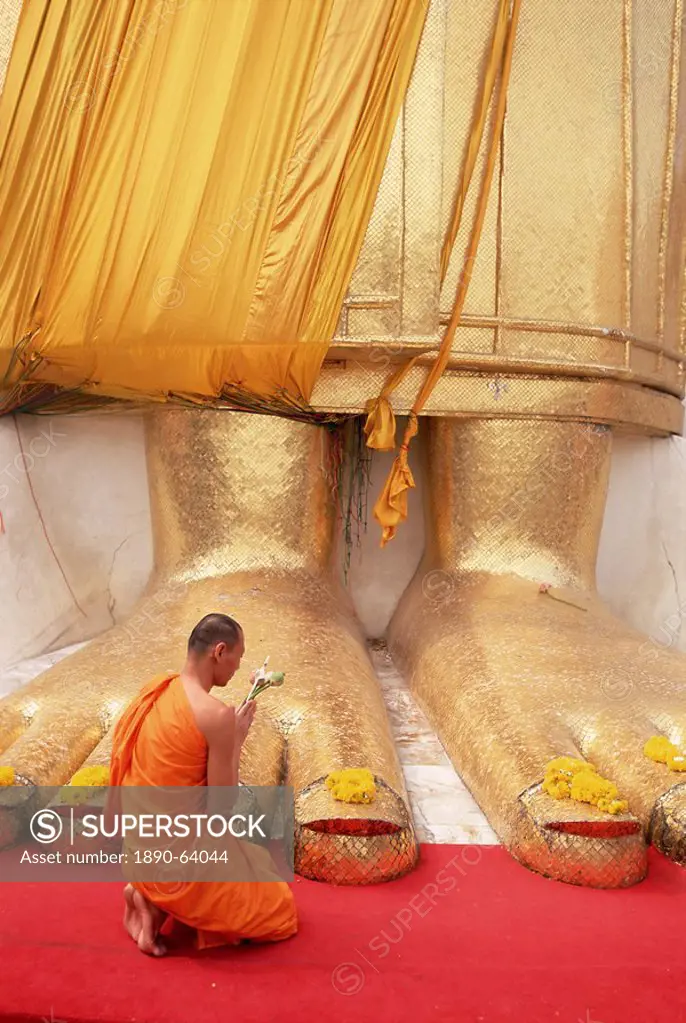 Buddhist monk kneeling in prayer at the feet of a statue of the standing Buddha, Wat Intharawihan, Bangkok, Thailand, Southeast Asia, Asia
