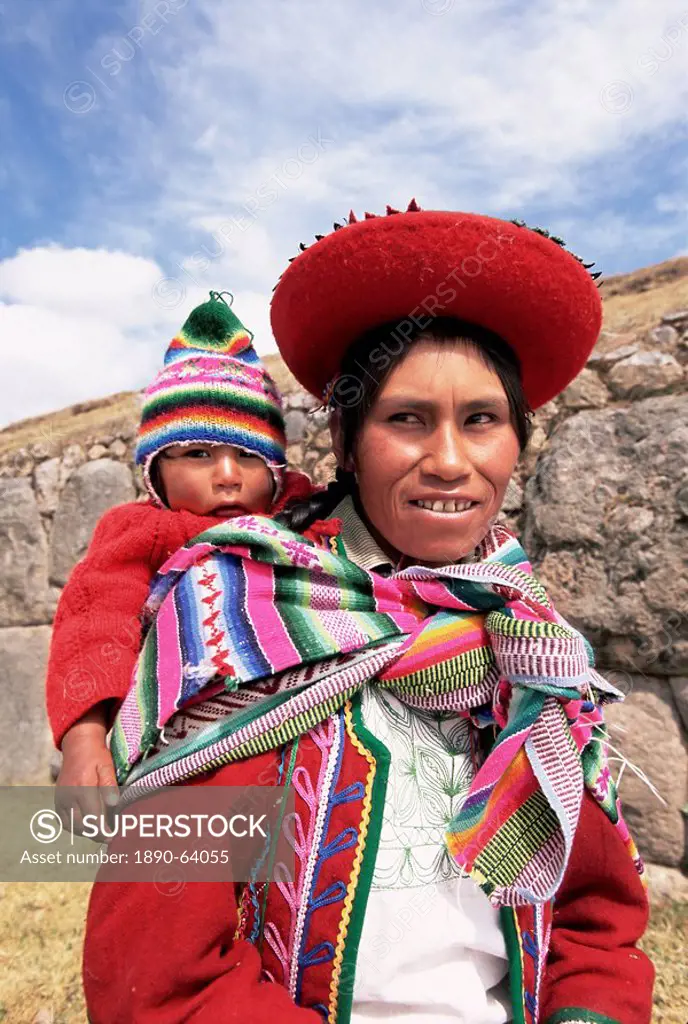 Portrait of a local woman in traditional dress, carrying her baby on her back, in front of Inca ruins, near Cuzco, Peru, South America