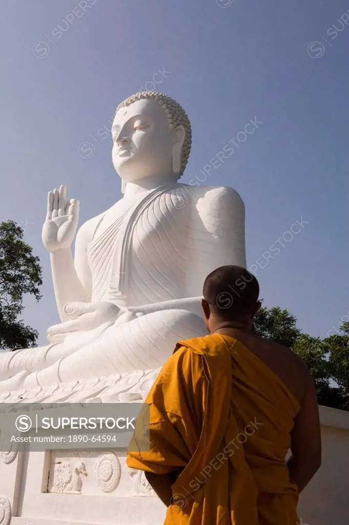 Monk standing in front of the great seated figure of the Buddha, Mihintale, Sri Lanka, Asia