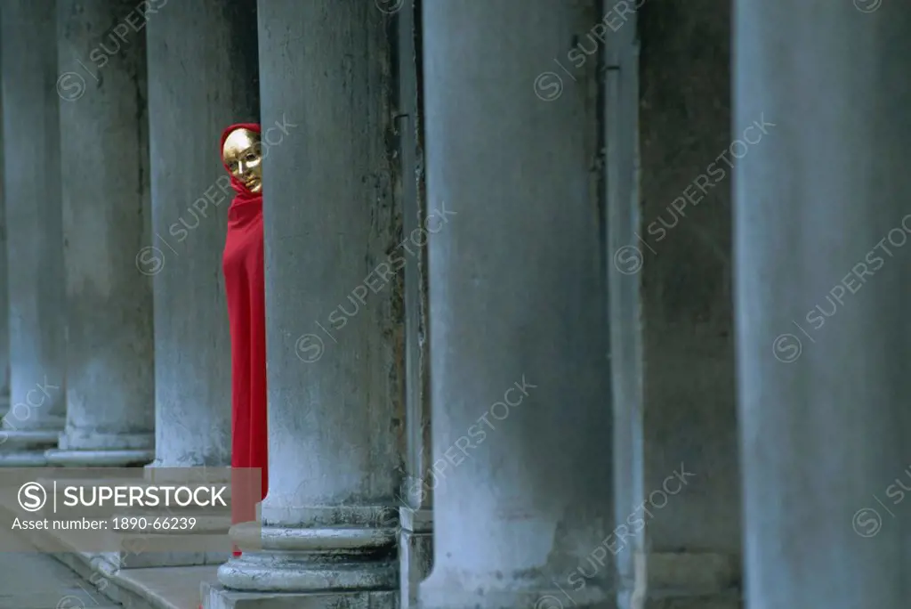 Carnival model in red cape and gold mask peering from columns in St. Mark´s Square, Venice, UNESCO World Heritage Site, Veneto, Italy, Europe