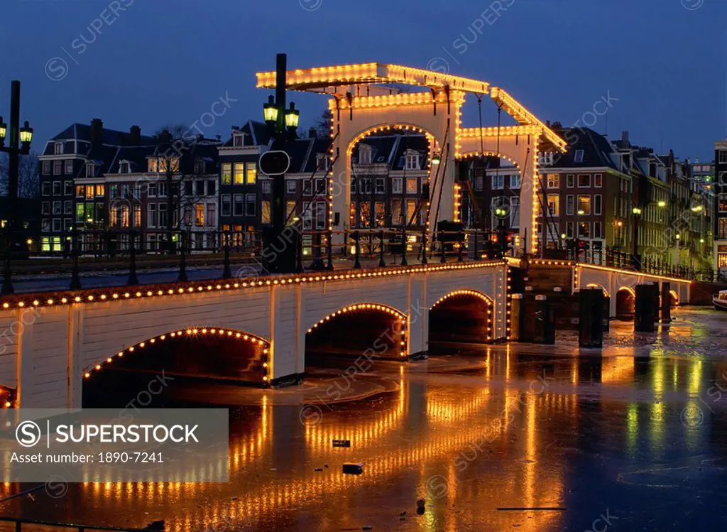 Lights on the Magere Brug Skinny Bridge reflected in the canal, in winter in Amsterdam, Holland, Europe