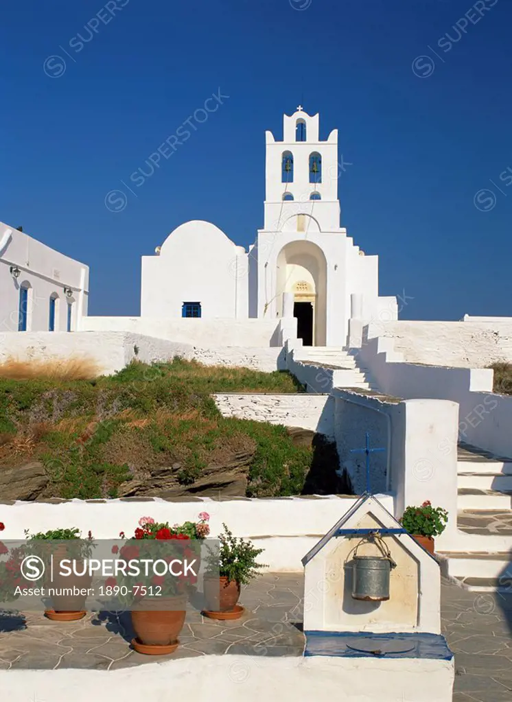 Pots of geraniums beside a well in front of the white walls and bell tower of the Monastery of Panagia Chrysopigi on Sifnos, Cyclades, Greek Islands, ...