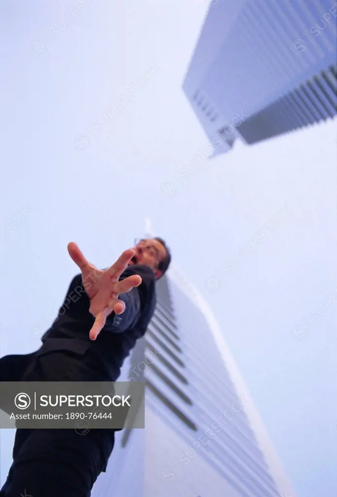 Stressed business man outdoors contemplating suicide, with hand reaching out, office blocks behind