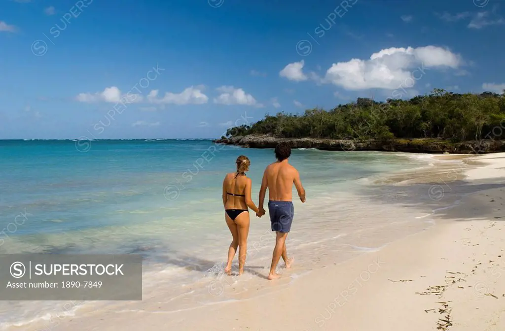 A couple walking along a small sandy beach near the Hotel Melia Rio de Oro, Carretera Guardalavaca, Cuba, West Indies, Central America