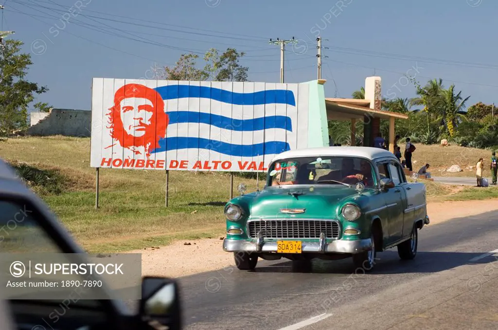 A vintage 1950´s American Chevrolet on the road near Trinidad passing a colourful revolutionary road sign, Cuba, West Indies, Central America