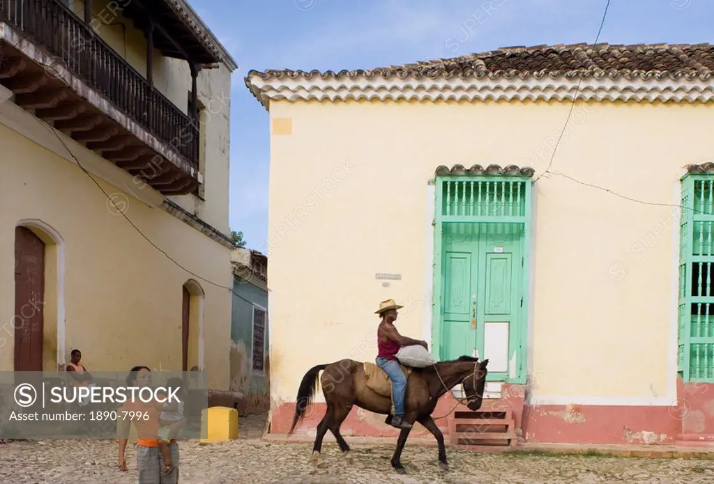 A cowboy riding a horse through the cobbled streets and a woman carrying her baby, Trinidad, Cuba, West Indies, Central America