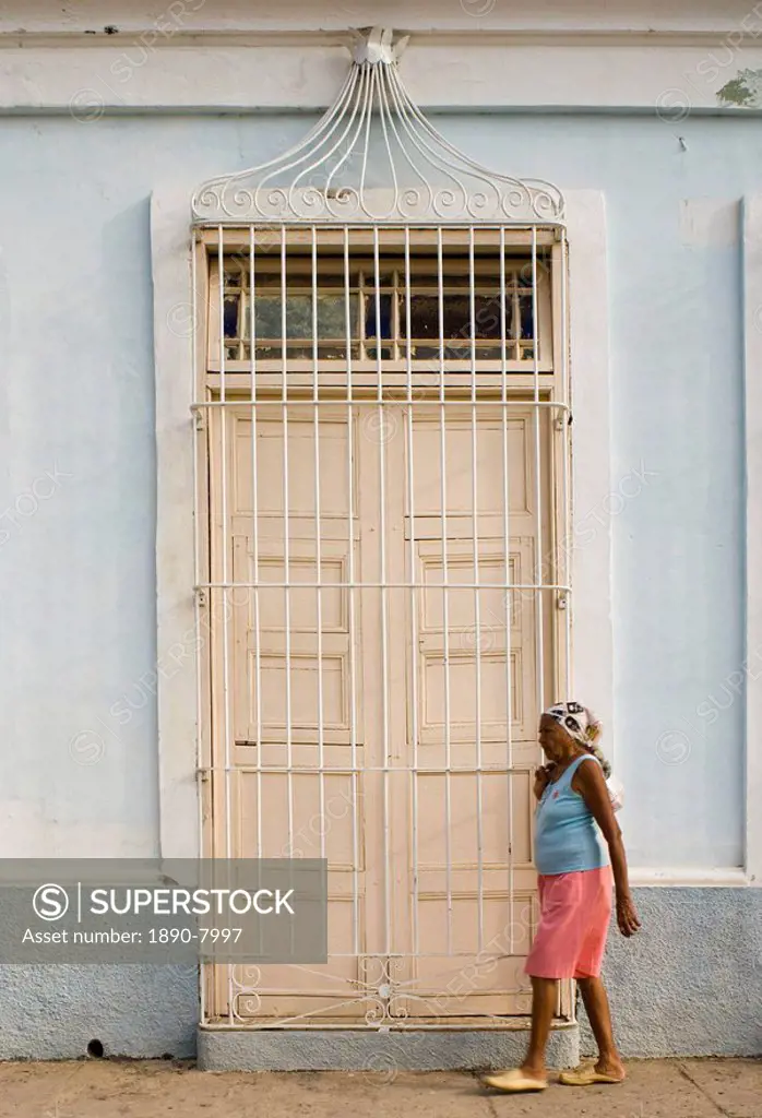 A woman walking past a typical door with ornate iron bars, Trinidad, Cuba, West Indies, Central America