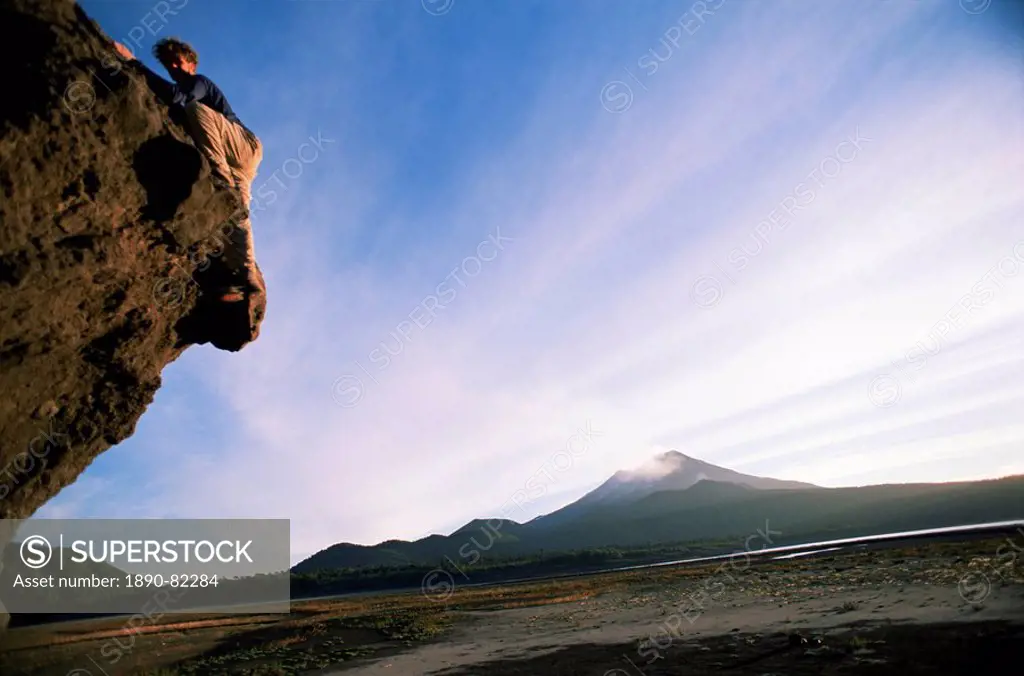 Rock climber attempts bouldering, and volcano in background, Conguillio National Park, Chile, South America