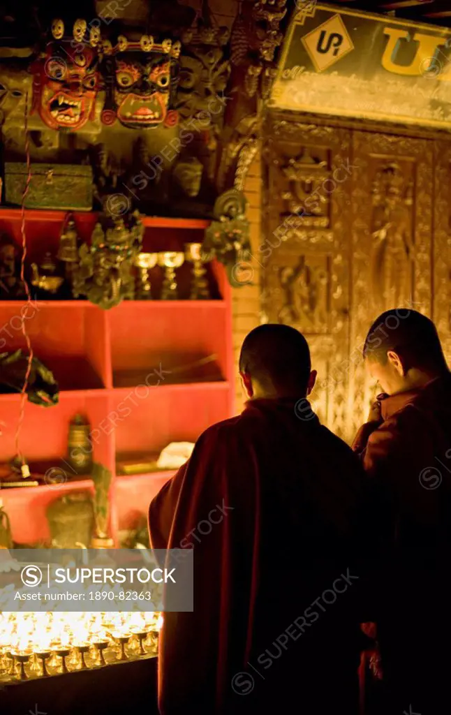 Monks light butter lamps on an auspicious night, watched by two fearsome masks, Boudha stupa, Bodhnath, Kathmandu, Nepal.