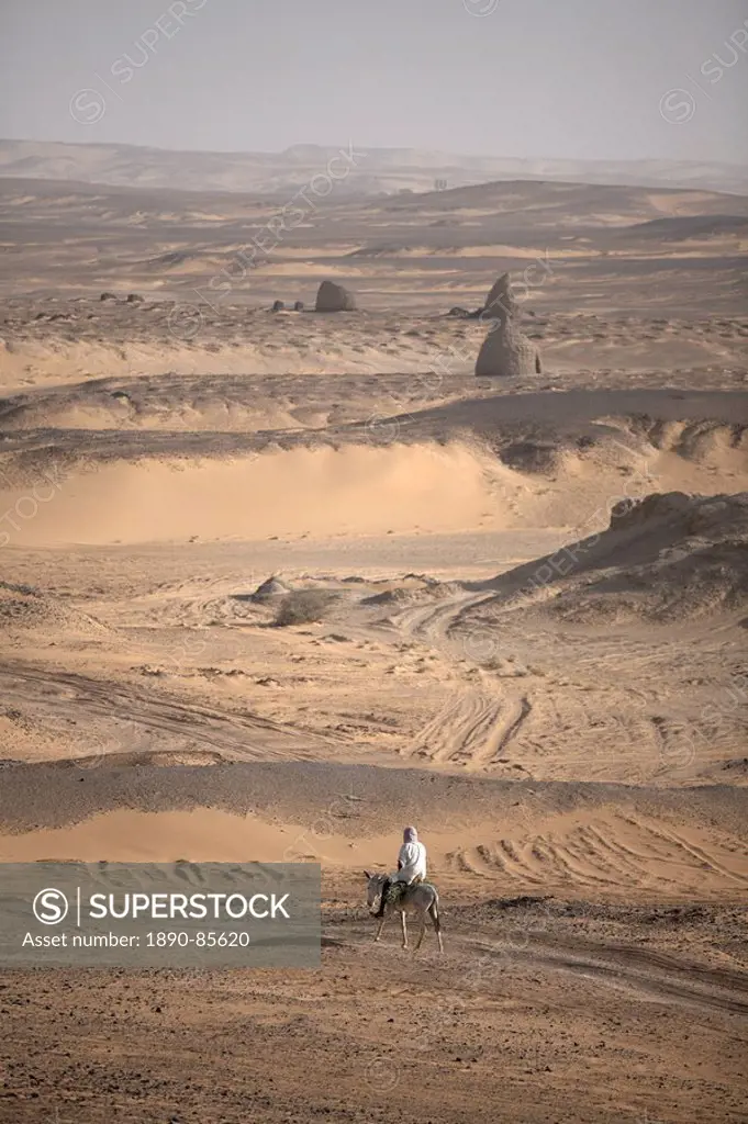 A man on mule_back traverses the desert around the ancient city of Old Dongola, Sudan, Africa