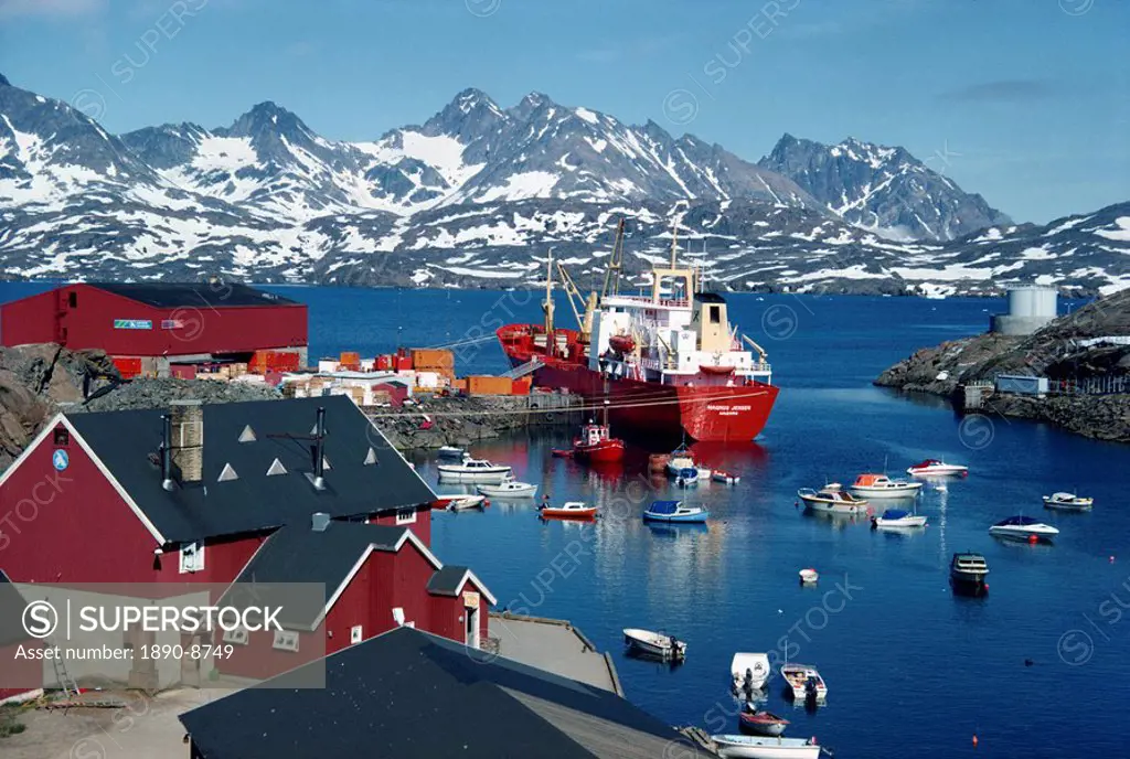 Cargo ship with freight on the quay, small boats in the harbour, and mountains in the background, at Ammassalik, east Greenland, Polar Regions