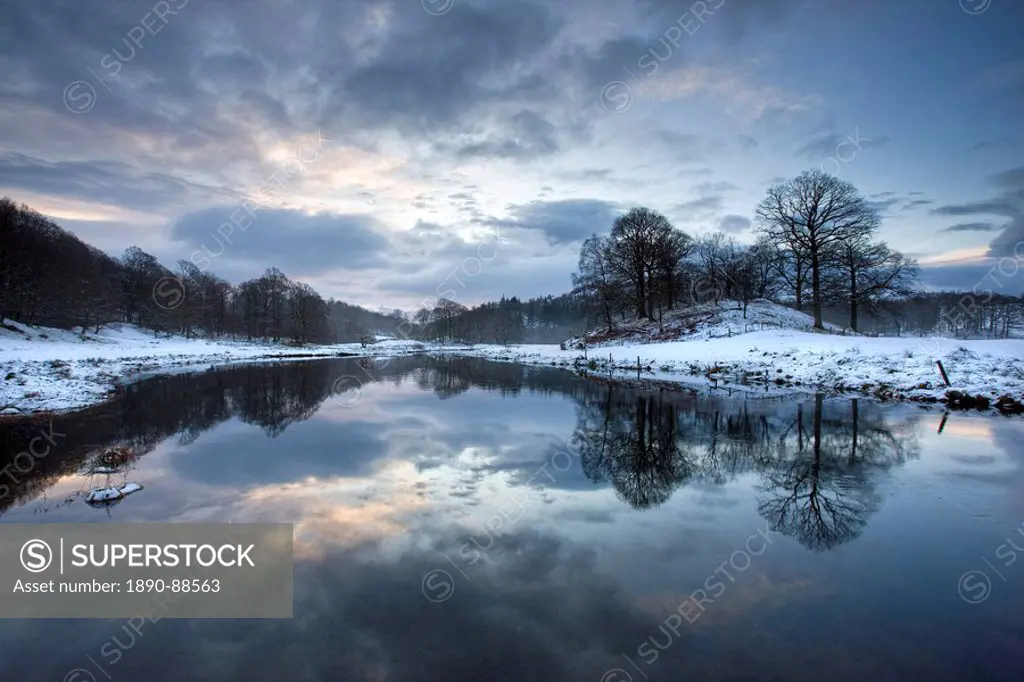 Winter view of River Brathay at dawn, under snow with reflections, near Elterwater Village, Ambleside, Lake District National Park, Cumbria, England, ...