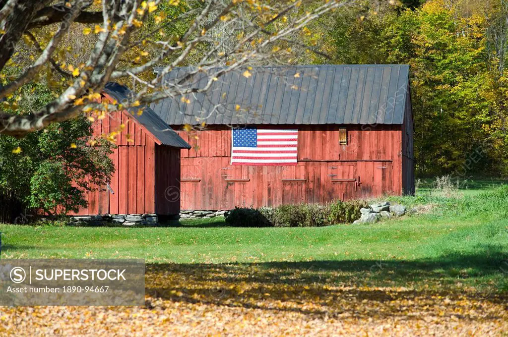 An old red barn with an American flag hanging on the side and autumn foliage on the hill behind, Vermont, New England, United States of America, North...