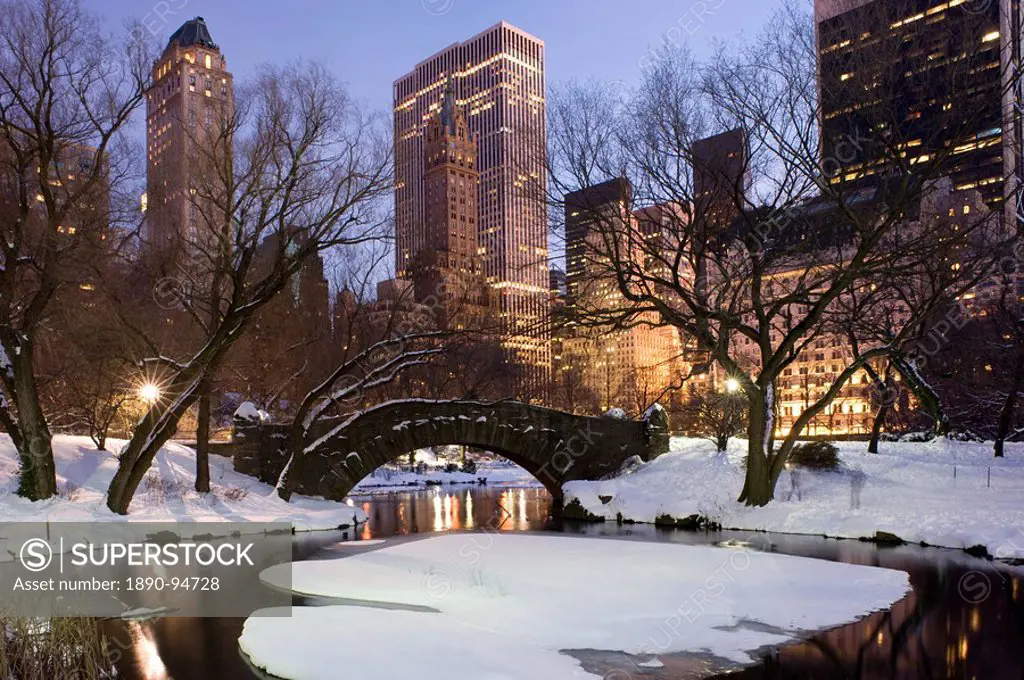 The Gapstow Bridge in Central Park after a snowstorm with skyscrapers behind at dusk, New York City, New York State, USA