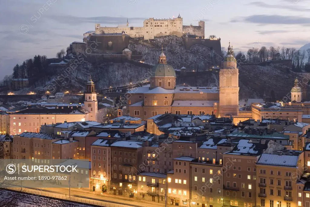 Snow covered Old Town with towers of Glockenspiel, Dom and Franziskanerkirche churches dominated by the fortress of Festung Hohensalzburg at twilight,...