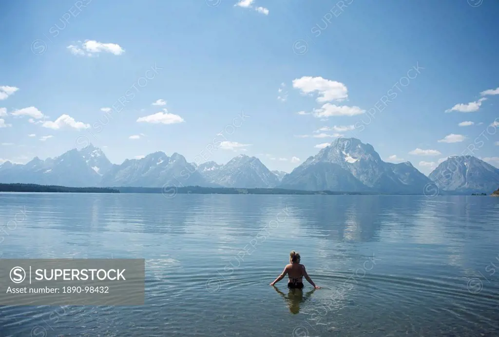 Woman wades in lake with Tetons in distance, Grand Teton National Park, Wyoming, United States of America, North America