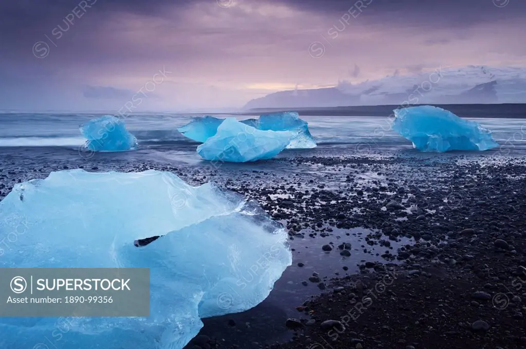 Icebergs washed ashore on Breidamerkursandur black sands, near Jokulsarlon glacial lagoon, Oraefajokull Vatnajokull glacier in the distance, East Icel...