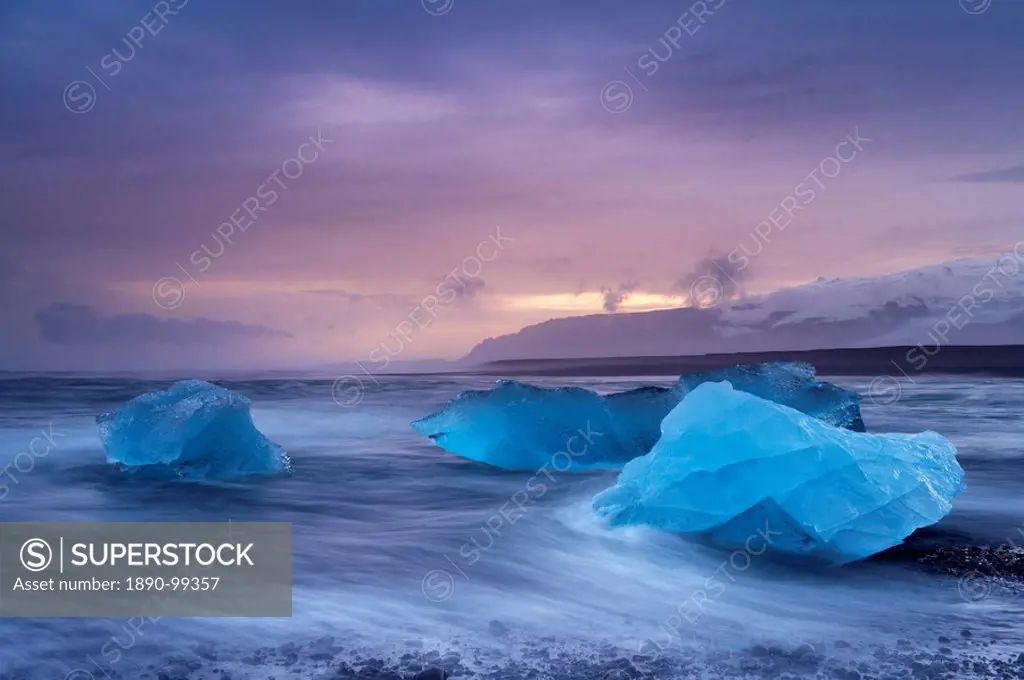 Icebergs washed ashore on Breidamerkursandur black sands, near Jokulsarlon glacial lagoon, Oraefajokull Vatnajokull glacier in the distance, East Icel...