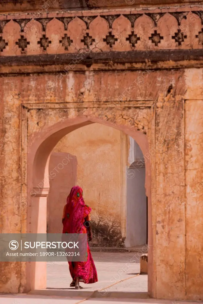 Lady in traditional dress walking through a gateway in the Amber Fort near Jaipur, Rajasthan, India, Asia
