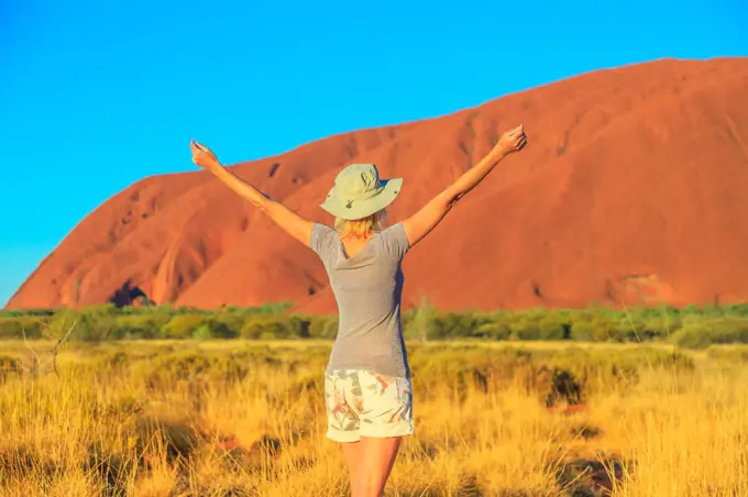 Carefree tourist woman with raised arms enjoys Uluru (Ayers Rock) at sunset in Uluru-Kata Tjuta National Park, UNESCO World Heritage Site, Northern Territory, Australia, Pacific