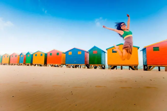 Laura Grier jumping in front of colorful beach huts, Muizenberg Beach, Cape Town, South Africa, Africa