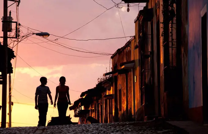 Two young people in silhouette at sunset on cobbled street with colourful orange sky behind, Trinidad, UNESCO World Heritage Site, Cuba, West Indies, ...