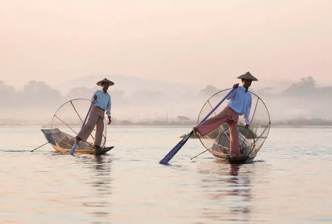 Intha 'leg rowing' fishermen at dawn on Inle Lake who row traditional wooden boats using their leg and fish using nets stretched over conical bamboo f...